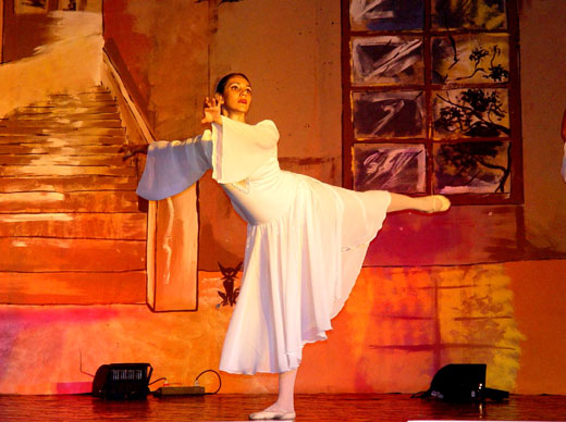 Балерина на сцене на фоне красных ярких декораций.